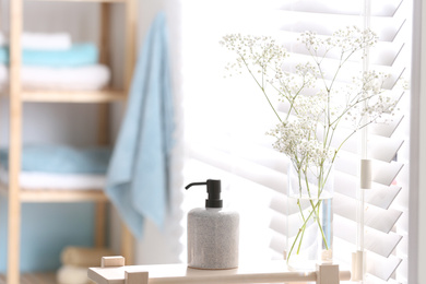 Soap dispenser and flowers on wooden stand in bathroom