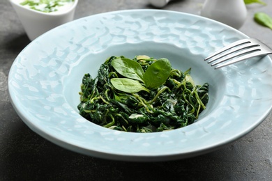 Photo of Plate with tasty spinach on grey  table, closeup. Healthy food