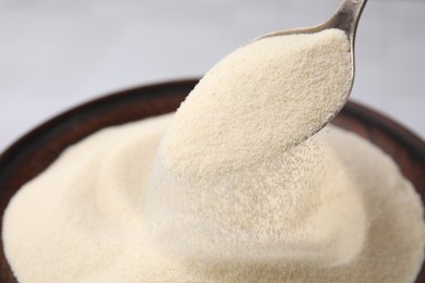 Photo of Pouring uncooked organic semolina from spoon into bowl, closeup