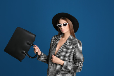 Photo of Beautiful young woman in sunglasses with stylish bag on blue background