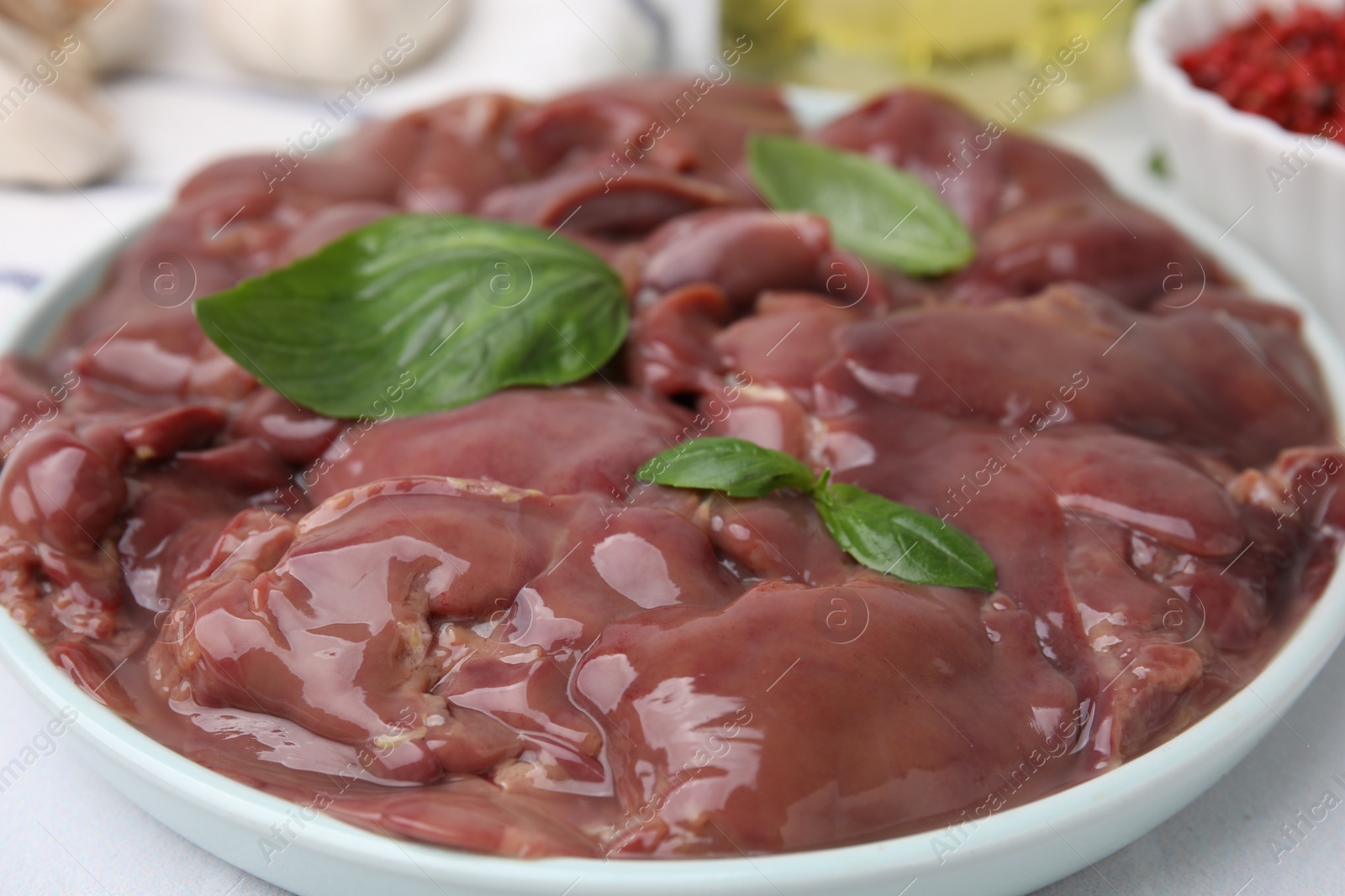 Photo of Plate of raw chicken liver with basil on white table, closeup