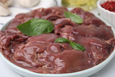 Photo of Plate of raw chicken liver with basil on white table, closeup