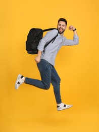 Emotional man with stylish backpack jumping on yellow background