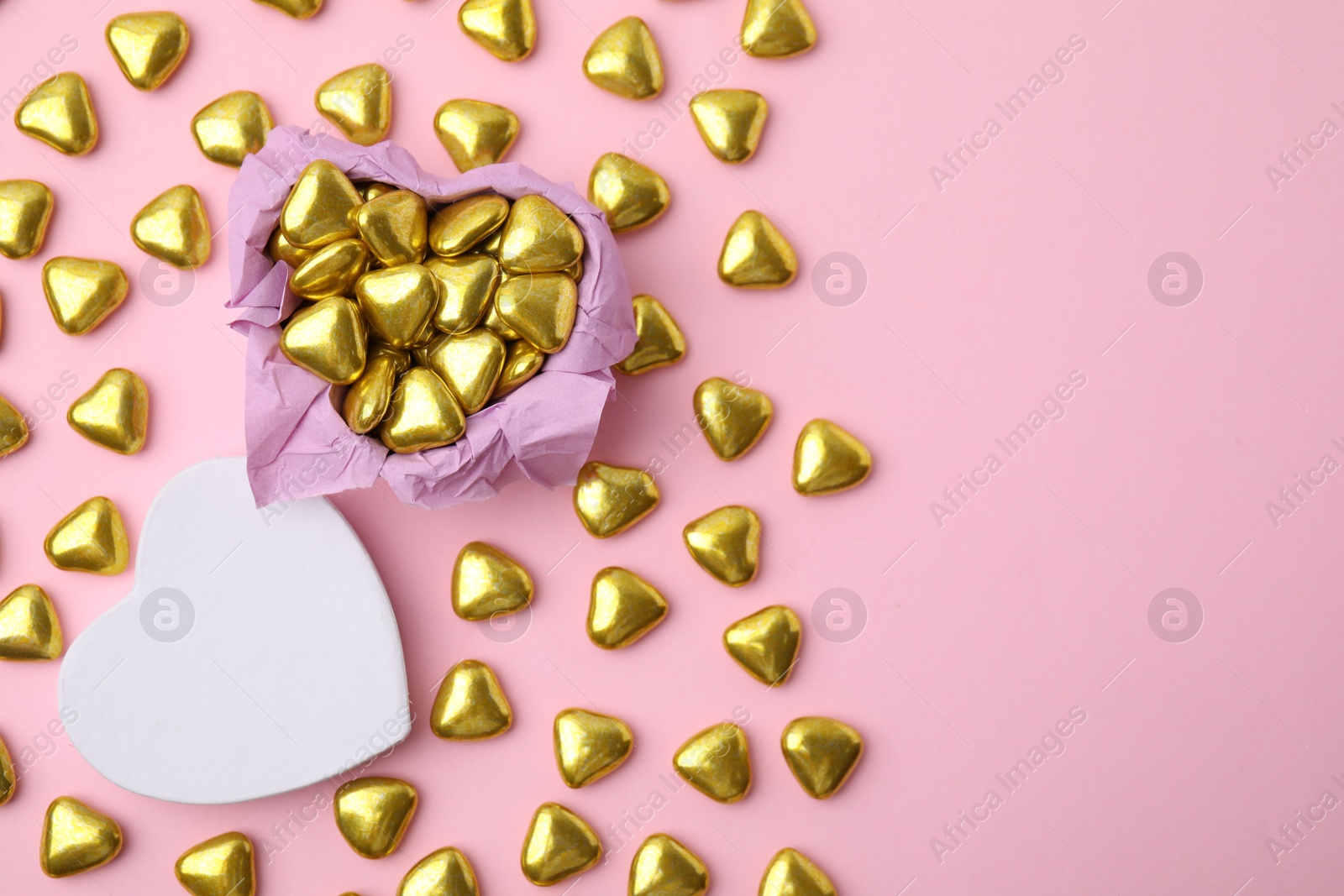 Photo of Box and delicious heart shaped candies on pink background, flat lay. Space for text