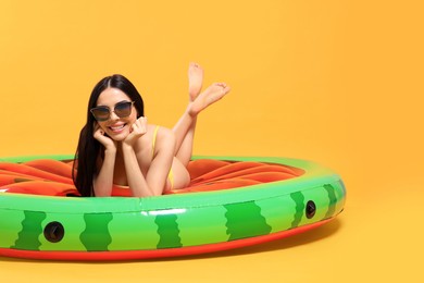 Photo of Happy young woman with beautiful suntan and sunglasses on inflatable mattress against orange background
