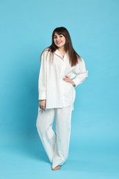 Photo of Happy woman wearing pyjama on light blue background