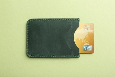 Leather card holder with credit card on light green background, top view