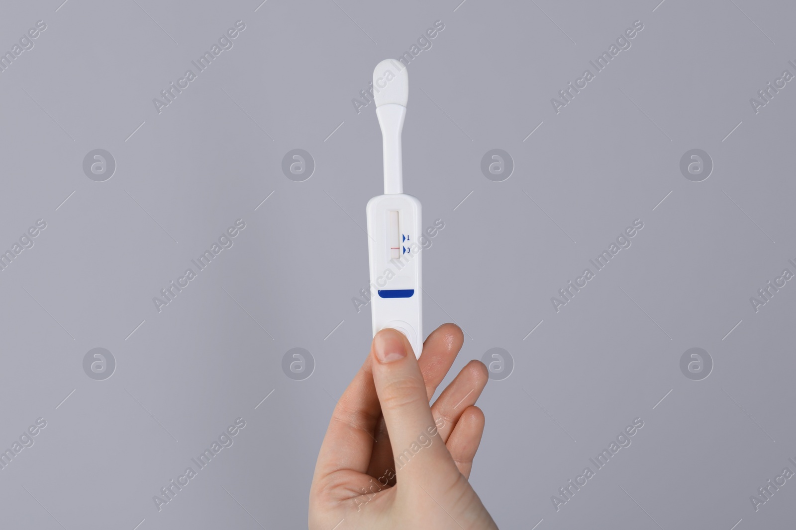 Photo of Woman holding disposable express test on light grey background, closeup