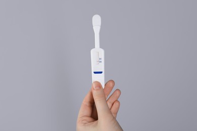 Photo of Woman holding disposable express test on light grey background, closeup