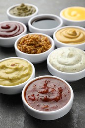 Photo of Many different sauces in bowls on grey table, closeup