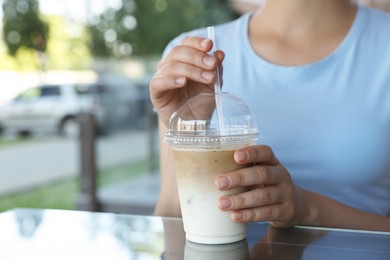 Photo of Woman with plastic takeaway cup of delicious iced coffee at table in outdoor cafe, closeup
