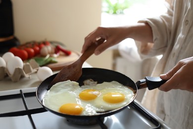 Photo of Woman cooking tasty eggs on frying pan in kitchen, closeup