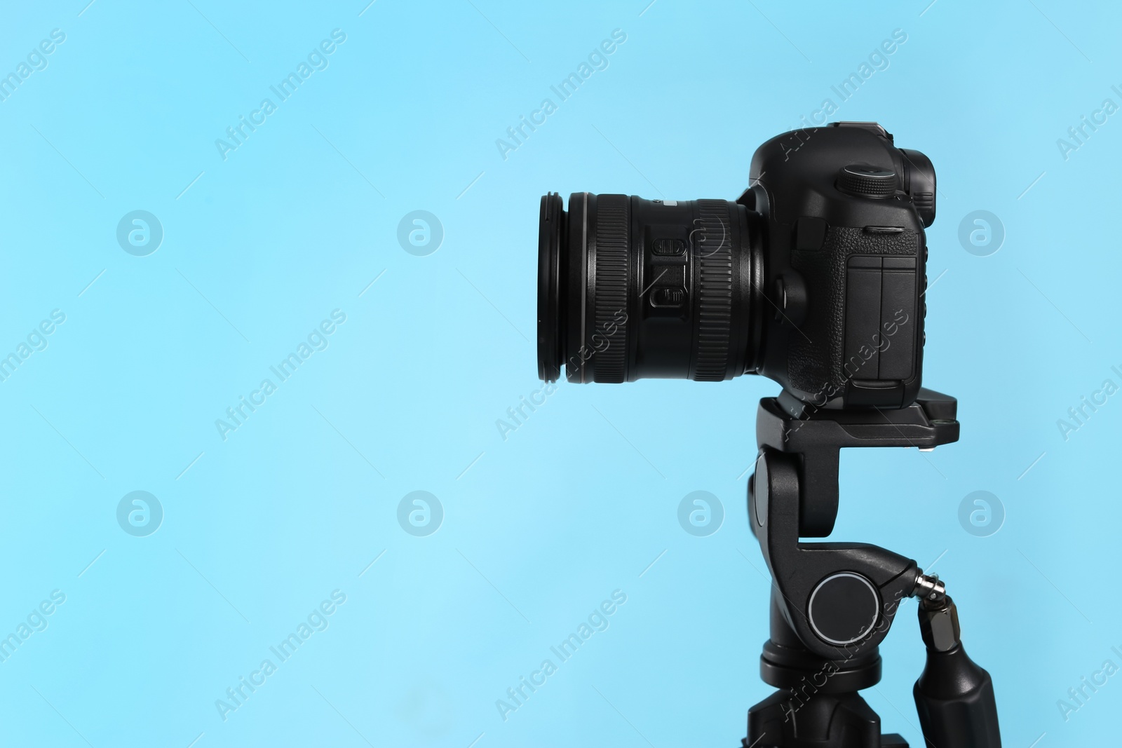 Photo of Modern tripod with professional camera on light blue background. Space for text