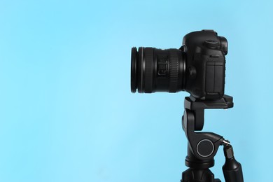 Modern tripod with professional camera on light blue background. Space for text