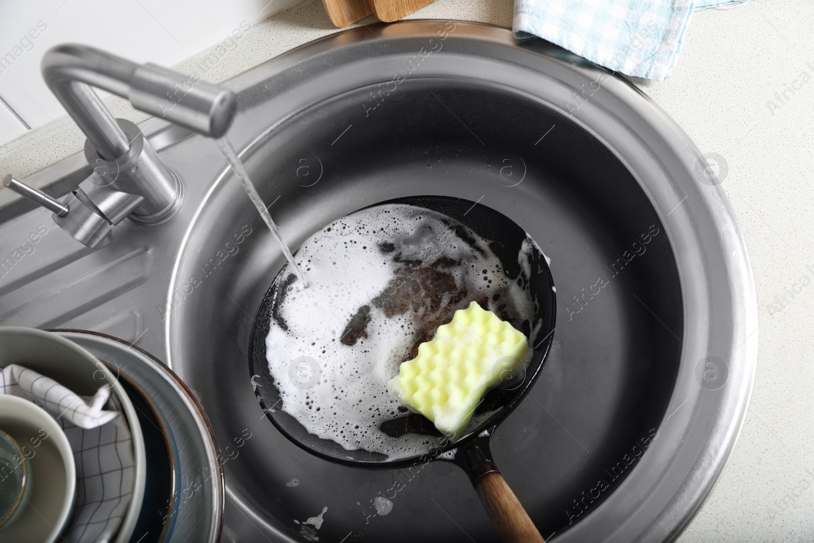 Photo of Dirty frying pan with sponge in kitchen sink, above view