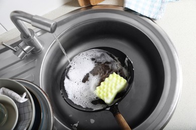 Photo of Dirty frying pan with sponge in kitchen sink, above view