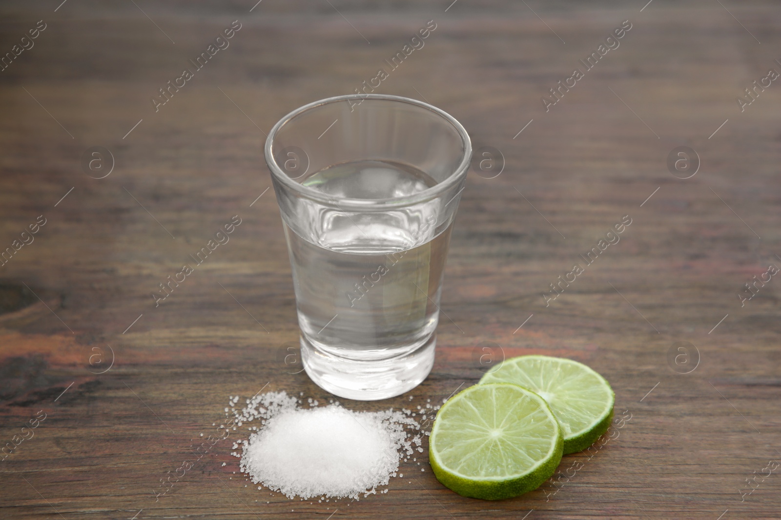 Photo of Mexican tequila shot with lime slices and salt on wooden table, closeup. Drink made from agave