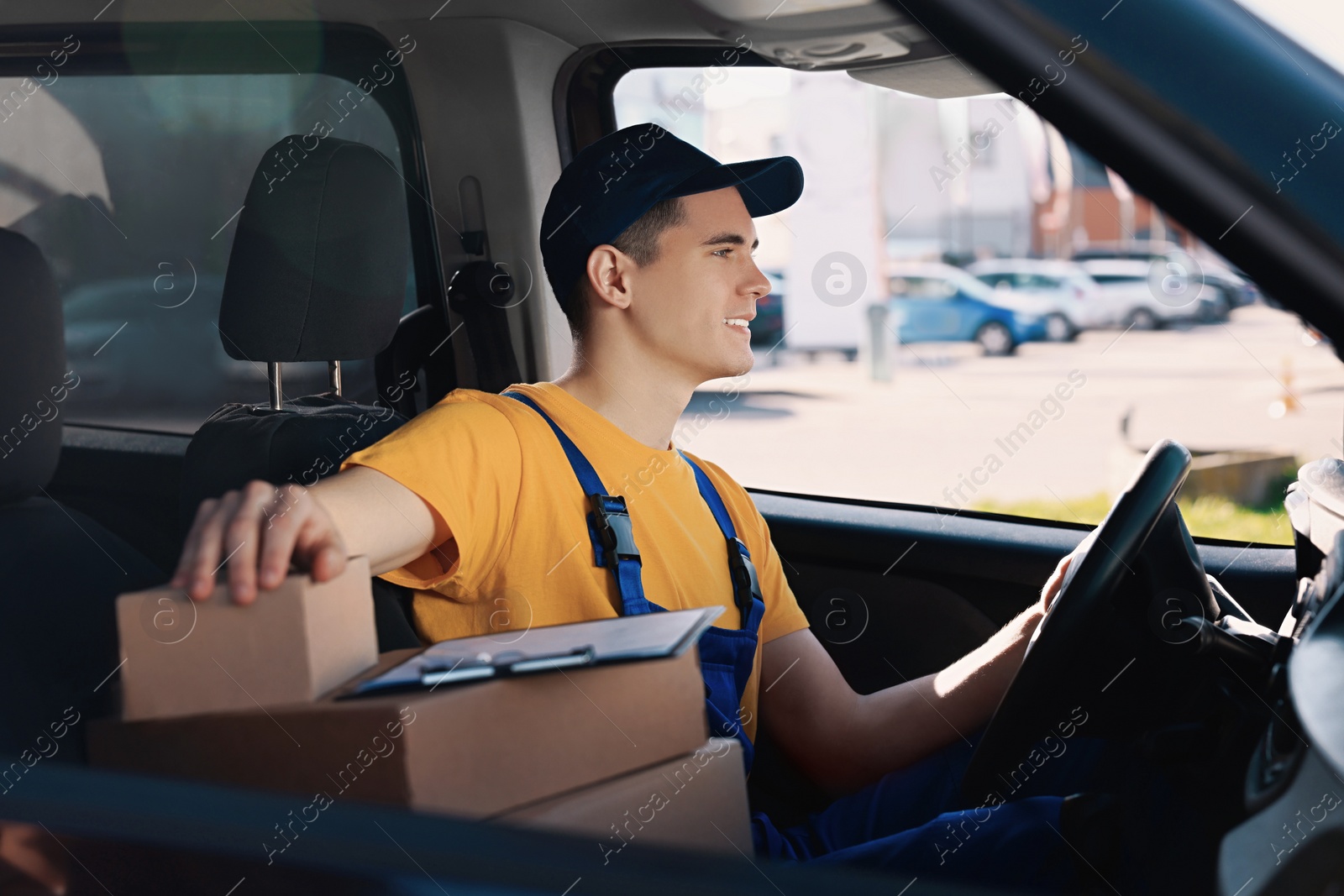 Photo of Courier with clipboard and parcels in car. Delivery service