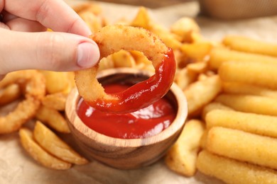 Photo of Woman dipping onion ring into bowl with tasty ketchup at table, closeup