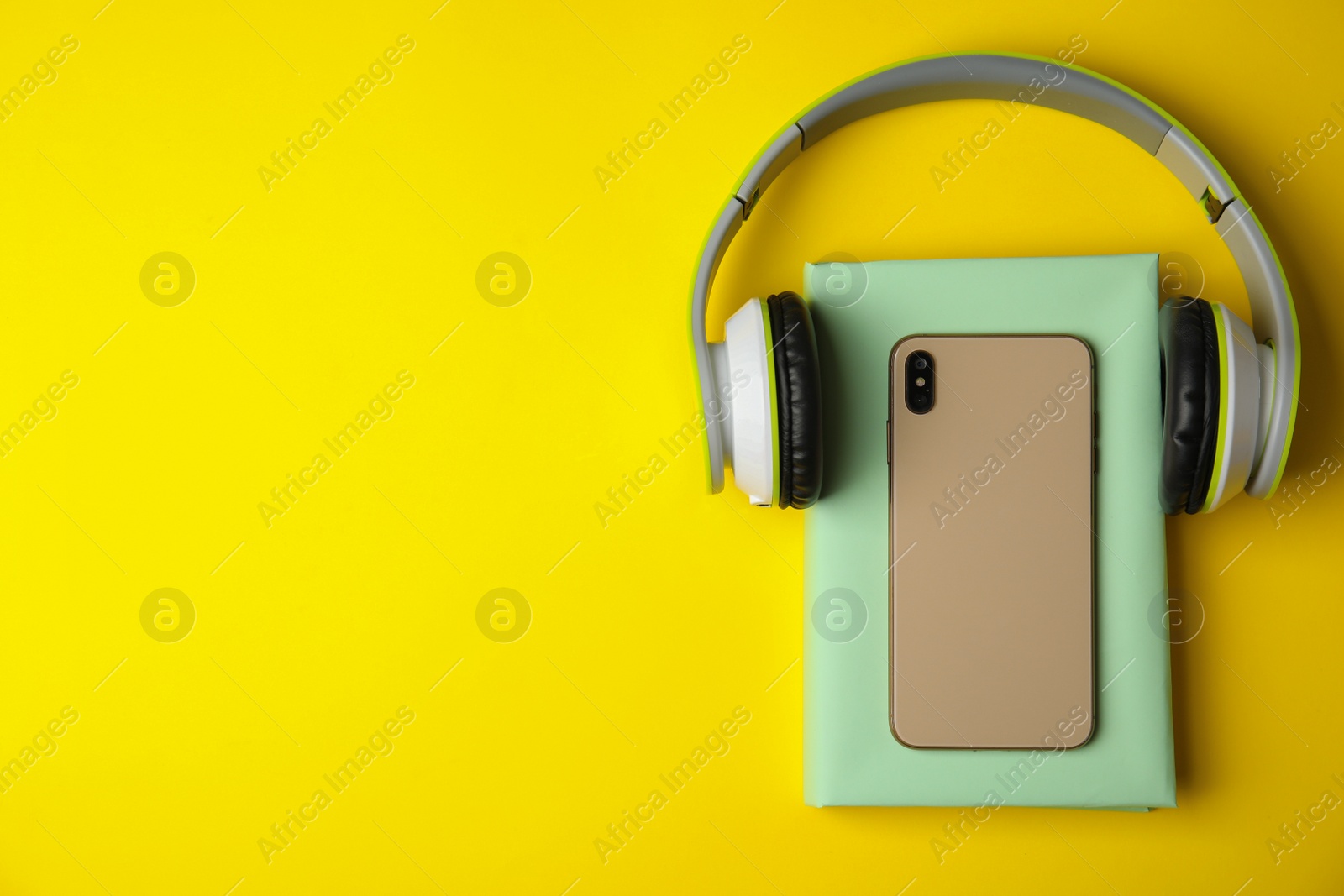 Photo of Book, mobile phone and headphones on yellow background, flat lay. Space for text