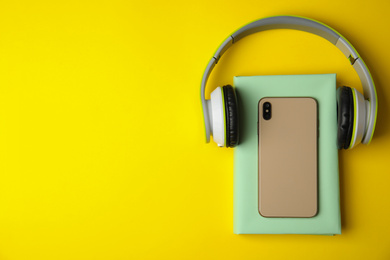 Book, mobile phone and headphones on yellow background, flat lay. Space for text