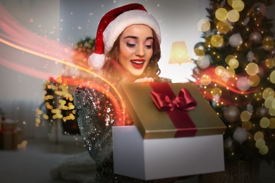Image of Beautiful woman in Santa hat opening Christmas gift at home