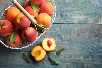 Photo of Fresh sweet peaches in metal basket on wooden table, flat lay