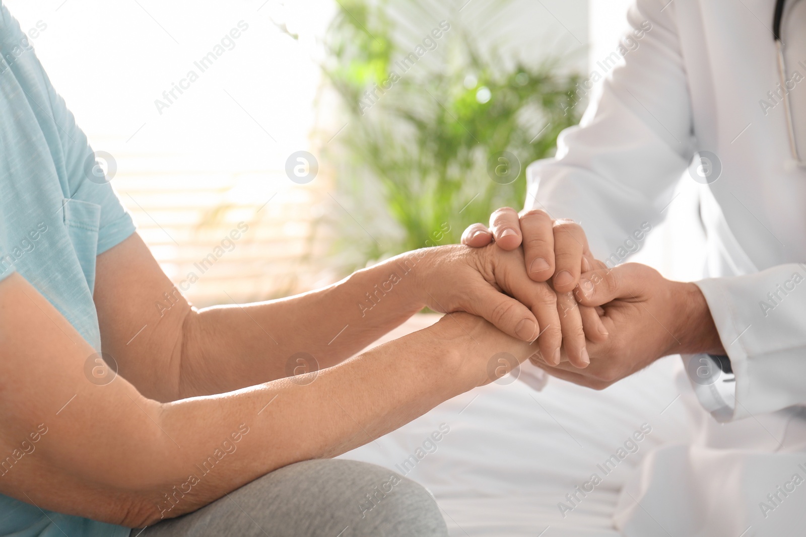 Photo of Doctor and senior patient holding hands in hospital, closeup