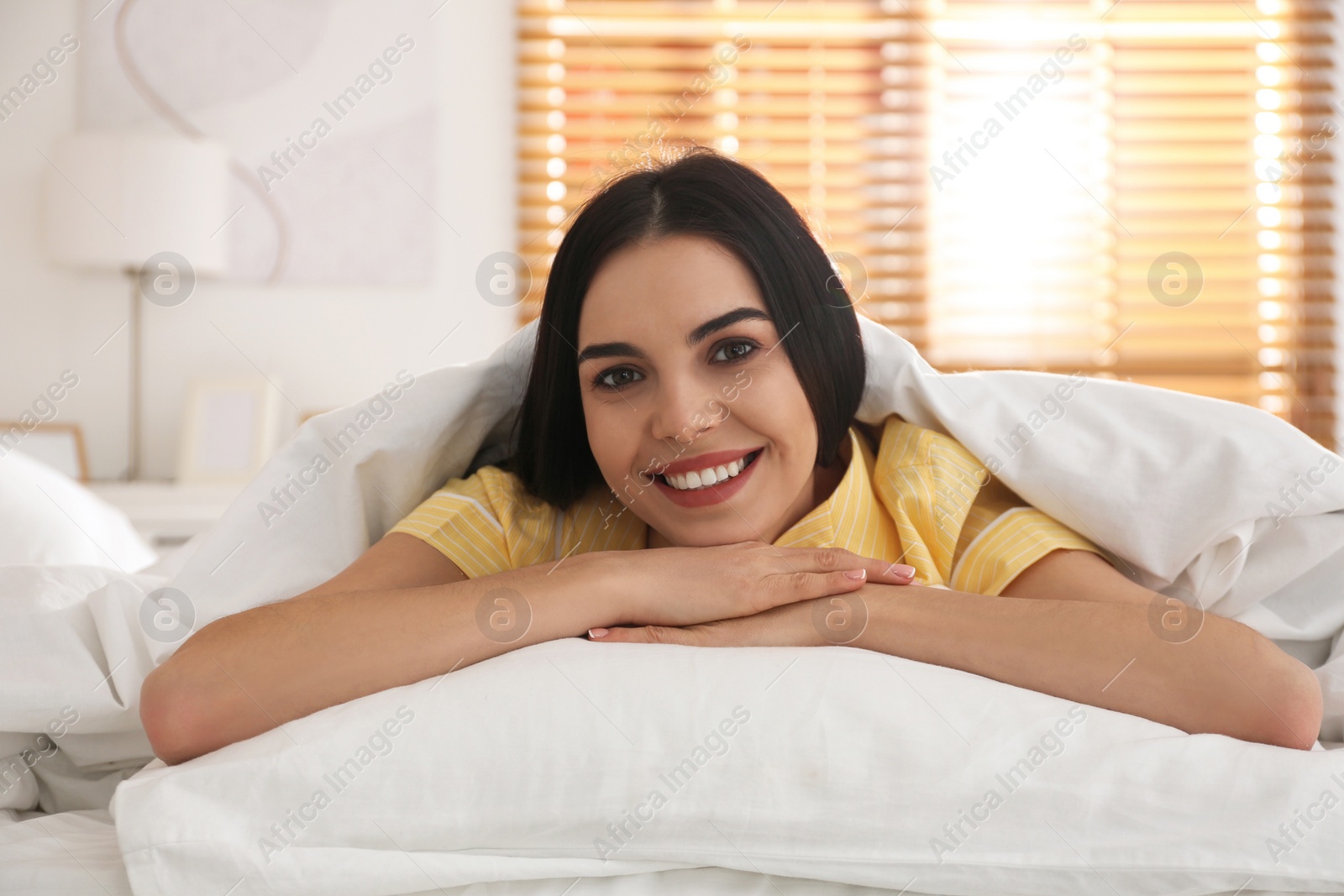 Photo of Young woman lying in bed with white linens at home