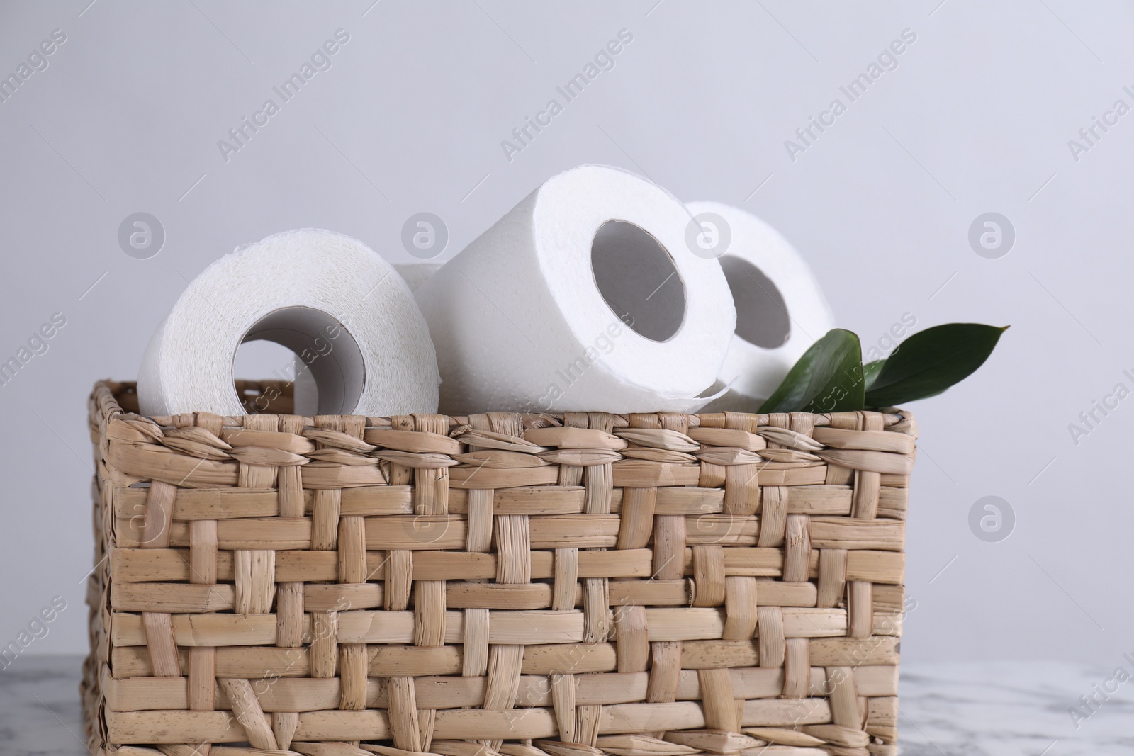 Photo of Toilet paper rolls and green leaves in wicker basket on white marble table