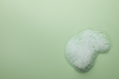 Photo of Drop of fluffy soap foam on green background, top view. Space for text