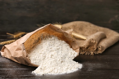 Photo of Paper bag with flour on wooden table