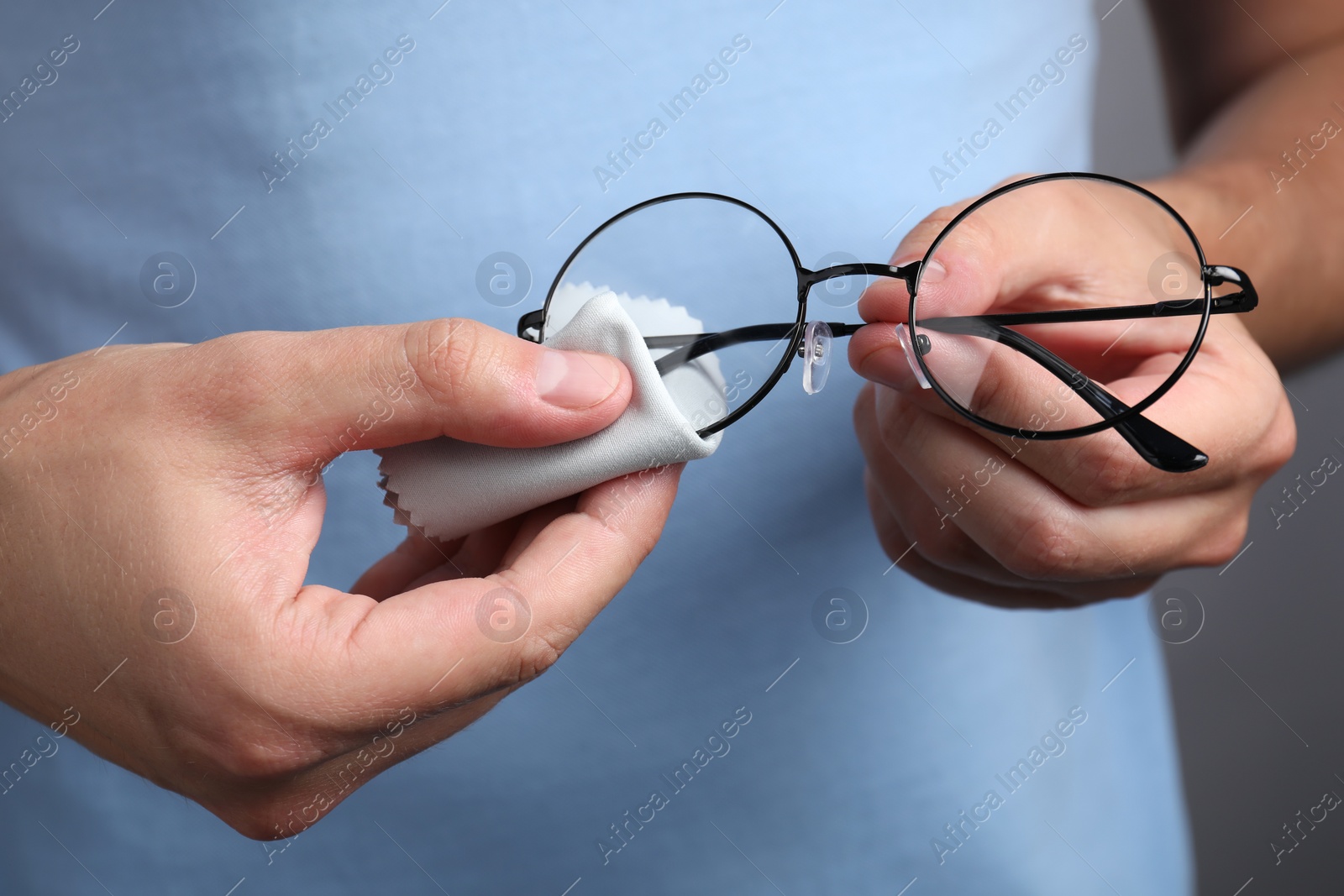Photo of Man wiping glasses with microfiber cloth on grey background, closeup