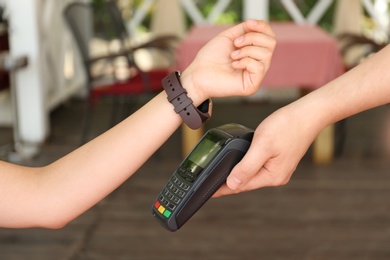 Photo of Woman using smartwatch for contactless payment in cafe, closeup