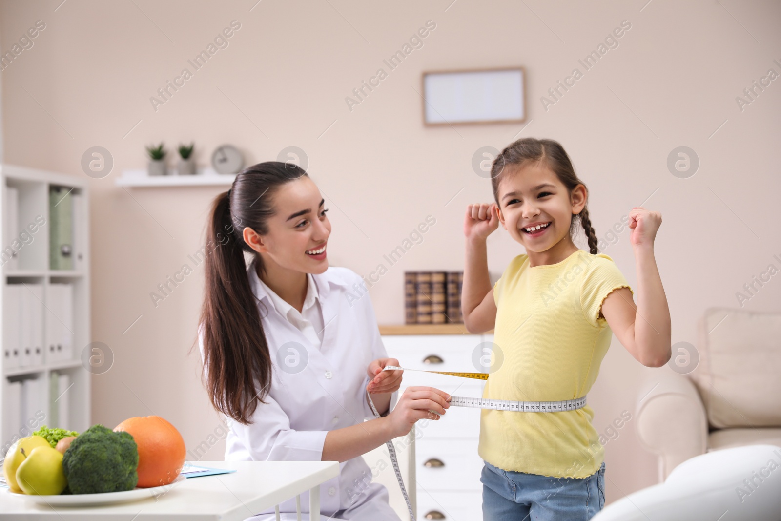 Photo of Professional nutritionist measuring waist of little girl in office