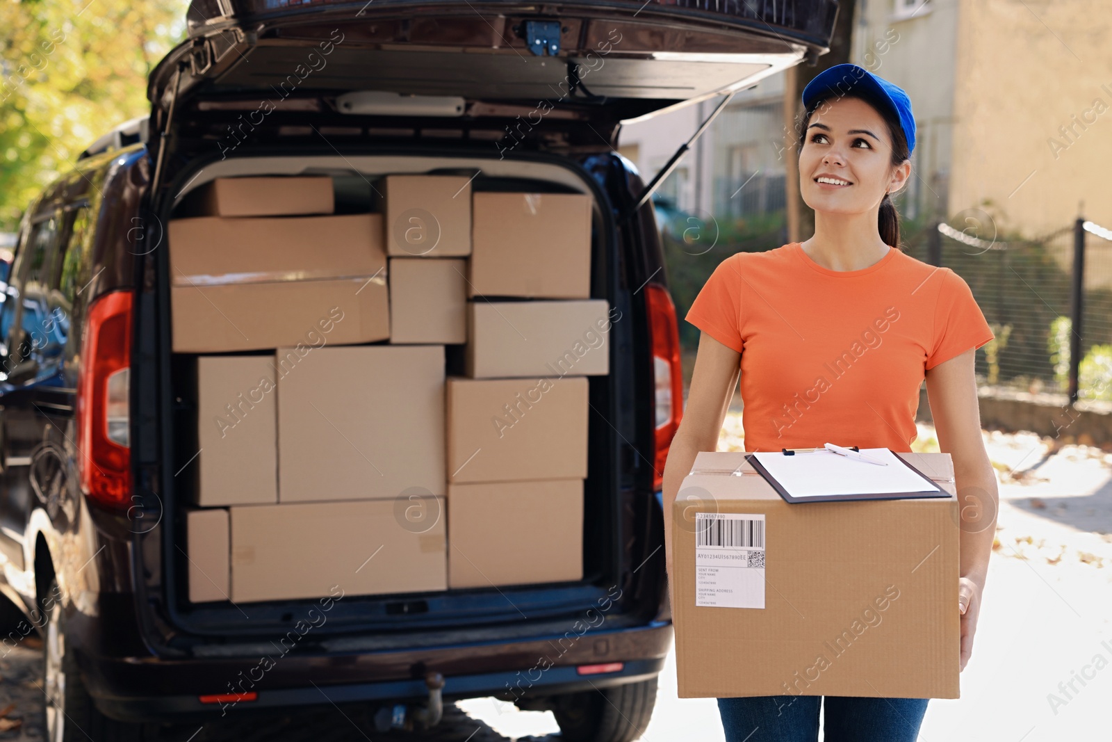 Photo of Courier holding package near delivery truck outdoors