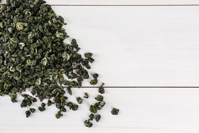 Photo of Heap of dried green tea leaves on white wooden table, top view. Space for text