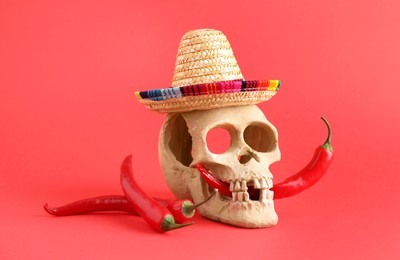 Photo of Human scull with Mexican sombrero hat and hot chili peppers on red background