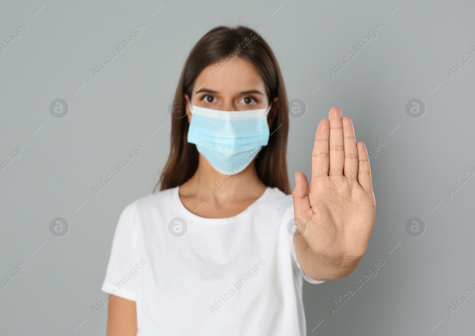 Photo of Woman in protective mask showing stop gesture on grey background. Prevent spreading of coronavirus