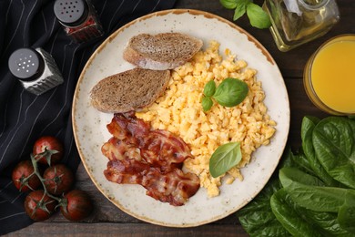 Delicious scrambled eggs with bacon and products on wooden table, flat lay
