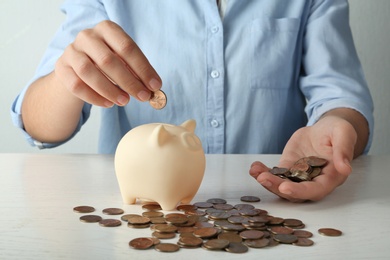 Photo of Young woman putting coin into piggy bank at wooden table, closeup view