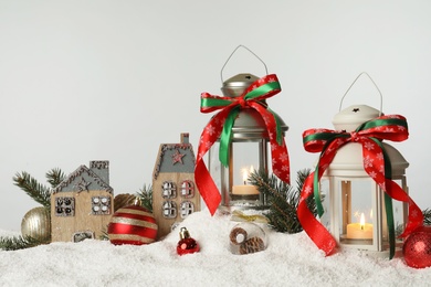 Photo of Decorative lanterns and Christmas decor on snow against light grey background