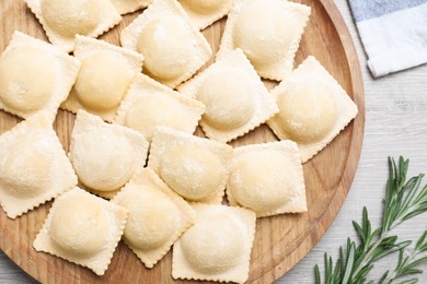 Photo of Uncooked ravioli and rosemary on white wooden table, flat lay