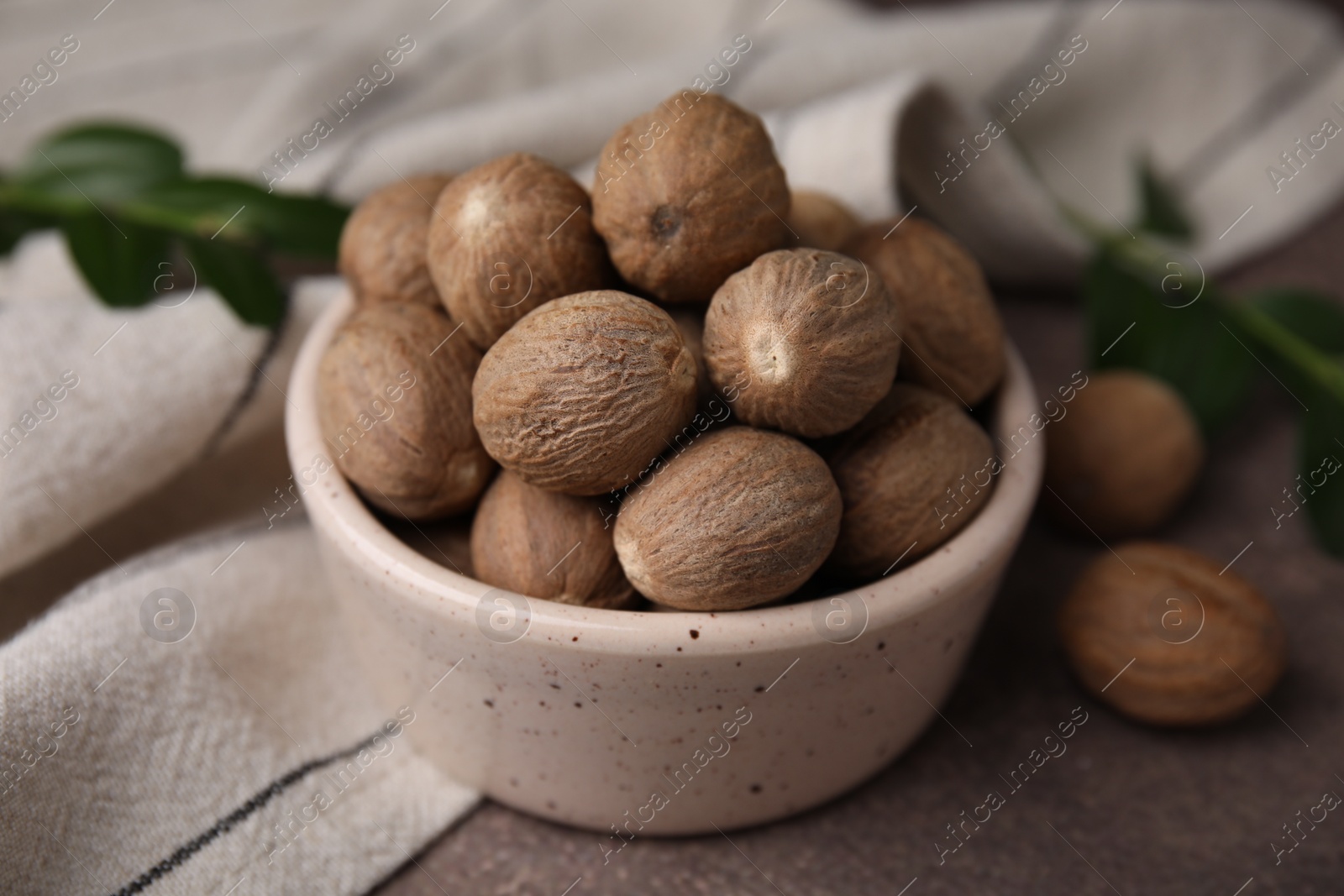 Photo of Whole nutmegs in bowl on brown table, closeup