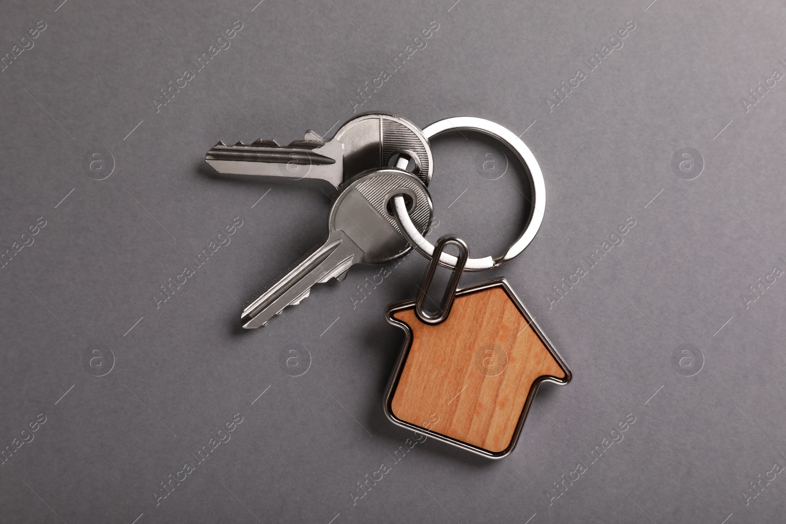 Photo of Keys with trinket in shape of house on grey background, top view. Real estate agent services