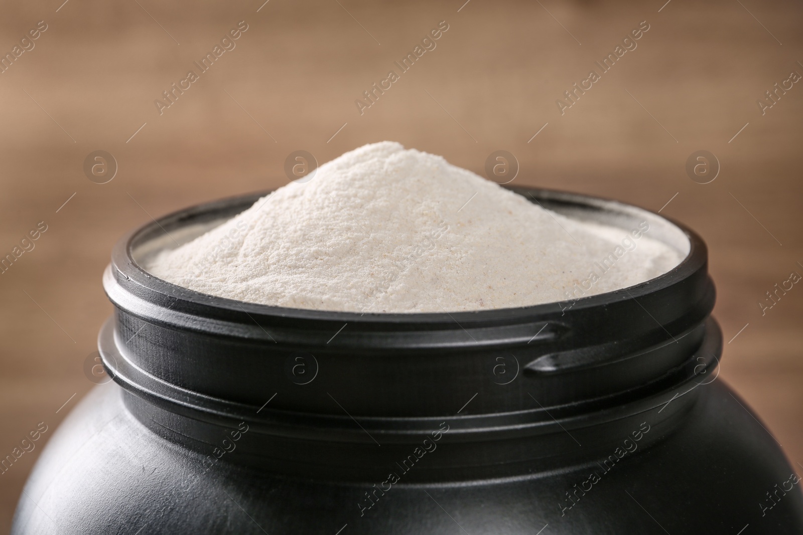 Photo of Black jar full of protein powder on brown background, closeup