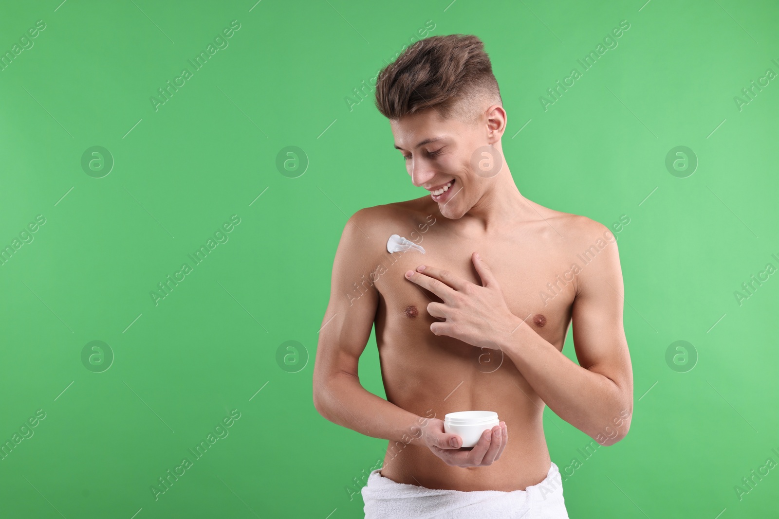 Photo of Handsome man applying moisturizing cream onto his shoulder on green background. Space for text