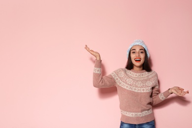 Young woman in warm sweater and knitted hat on color background. Christmas celebration