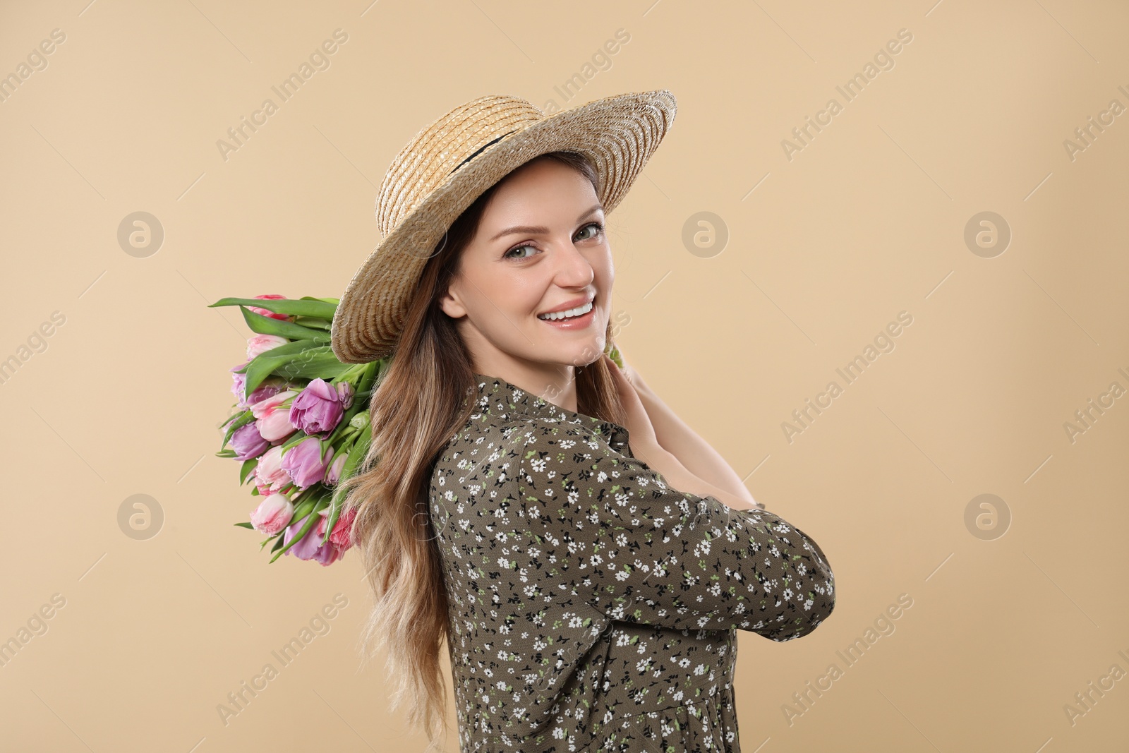 Photo of Happy young woman in straw hat holding bouquet of beautiful tulips on beige background