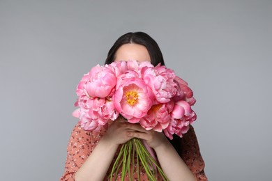 Young woman covering her face with bouquet of peonies on light grey background